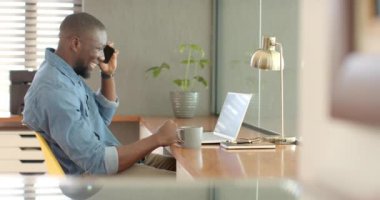 Evde çalışan, akıllı telefon ve dizüstü bilgisayar kullanan profesyonel bir erkek. Uzaktan çalışma, telekomünikasyon, serbest çalışma, üretkenlik, teknoloji, ev ofisi, değiştirilmemiş, yaşam tarzı