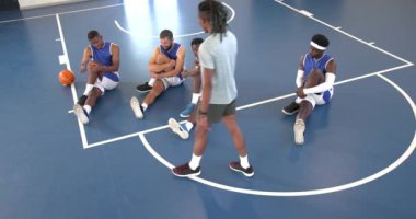 Çok ırklı erkek basketbol oyuncuları spor salonunda antrenörle bacaklarını esnetiyorlar. spor, yaşam tarzı ve etkinlik.