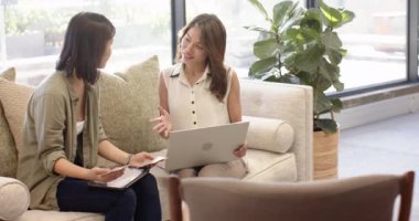 İç dizayn fikirlerini tartışıyorlar, iki çok ırklı kadın ofiste dizüstü bilgisayar kullanıyor ve notlar alıyor. işbirliği, beyin fırtınası, yaratıcılık, çalışma alanı, planlama, takım çalışması