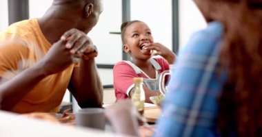Afro-Amerikan ailesi yemek masasında yemek yiyor, gülümsüyor ve konuşuyor. Yemek zamanı, kaynaşma, sohbet, mutluluk, birliktelik, toplanma.