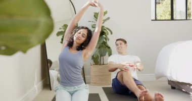 Evde dinlenen, yerde oturan ve birlikte gülümseyen çok kültürlü genç bir çift. Rahatlama, yaşam tarzı, rahatlık, kapalı alan, mutluluk, bağ.