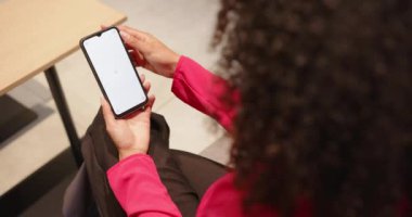 Akıllı telefonu tutan, pembe bluzlu bir kadın masa başında otururken ekranı kontrol ediyor. Teknoloji, cep telefonu, aygıt, ofis, çalışma alanı, iletişim