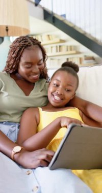 Dikey video: Koltukta dinlenirken tablet kullanan gülümseyen anne ve kız. Aile, bağ, teknoloji, rahatlama, ev, ebeveynlik