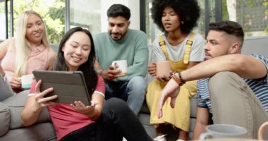 Tablet 'te video izliyoruz, bir grup genç arkadaş birlikte rahatlıyor ve gülümsüyor. Arkadaşlık, teknoloji, eğlence, eğlence, bağlanma, rahatlama.
