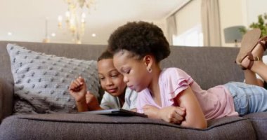 Çocuklar kanepede yatar, gülümser ve evde birlikte tablet izlerler. Çocukluk, teknoloji, kardeşler, eğlence, kaynaşma, eğlence