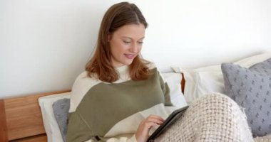 Yatakta dinlenen, tablette kitap okuyan ve rahat battaniyenin keyfini çıkaran bir kadın. Rahatlama, rahatlık, teknoloji, rahatlık, dijital, yaşam tarzı