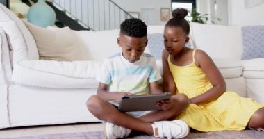Yerde otururken, Afro-Amerikan kardeşler oturma odasında tablet kullanıyor, oynuyorlar. technology, childhood, digital, home, interactive, education