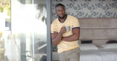 Evdeki rahat yatak odasında elinde kahve fincanı tutan gülümseyen adam. Yaşam tarzı, sabah, rahatlama, konfor, ev içi, günlük, boş, değişmemiş, yaşam tarzı