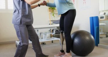 Fizyoterapist, protez bacaklı bir kadına egzersiz topunda yardım ediyor. Rehabilitasyon, fizyoterapi, sağlık, terapi, denge, hareketlilik