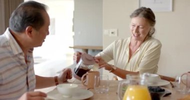 Kahvaltının tadını çıkarıyor, kıdemli çift masada kahve fincanlarıyla gülüyor ve kadeh kaldırıyor. Yaşlılar, yaşam tarzı, bağlılık, birliktelik, mutluluk, yemek, değişmemiş, yavaş çekim