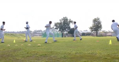 Çok ırklı erkek kriket oyuncularından oluşan takım sahada kriket beyazları giyerek antrenman yapıyor. Spor, etkinlik, takım çalışması, antrenman ve kriket.