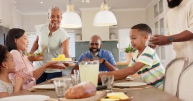 Çeşitli bir aile yemek masasının etrafında toplandı, gülümsüyor ve etkileşime giriyorlardı. Modern, aydınlık bir mutfakta bir sürahi limonata ve mısır koçanının üstünde, değiştirilmemiş.