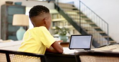 Modern evdeki masada otururken tablet kullanan sarı tişörtlü çocuk, boşluğu kopyala. Teknoloji, çocuk, kapalı alan, öğrenme, yaşam tarzı