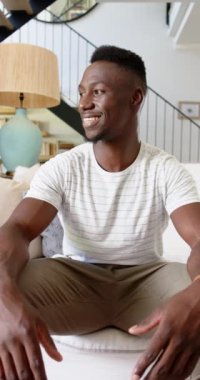 Dikey video: Oturma odasında kanepede oturan gülümseyen adam, rahatlamış aile zamanının tadını çıkarıyor. Rahatlama, rahatlama, mutluluk, ev, rahatlık, birliktelik.