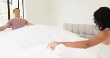 Pijamalı, gülümseyen bir adam Asyalı bir kadınla evde, parlak bir yatak odasında sevişiyor. Yurt içi, sabah, rutin, çok ırklı çift, mutluluk, yaşam tarzı