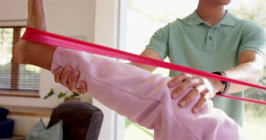 Fizyoterapist, direnç bandı kullanarak yaşlı kadına bacak egzersizi yaptırıyor. Fizyoterapi, rehabilitasyon, sağlık, yardım, fitness, terapi