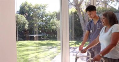 Erkek fizyoterapist Walker 'ın parlak odasında gülümseyen yaşlı kadına yardım etmek. Yardım, yaşlılar, destek, sağlık, fizyoterapi, rehabilitasyon