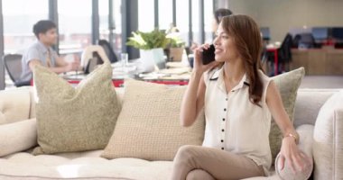 Akıllı telefondan konuşmak, modern ofis ortamında koltukta oturan bir kadın. İş, iletişim, teknoloji, profesyonel, işyeri, rahatlama