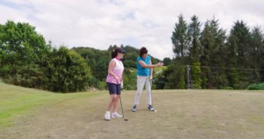 Kadın golfçüler konuşuyor, golf oynuyor ve golf sahasında topa vuruyor. spor, yaşam tarzı, golf ve etkinlik.