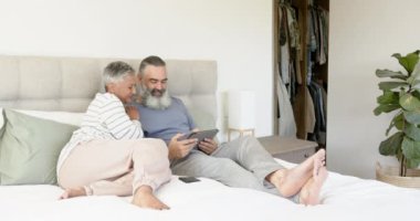 Yatakta dinlenen, tablet kullanan ve birlikte gülümseyen yaşlı çift. Yaşlılar, teknoloji, dijital aygıt, yatak odası, mutluluk, arkadaşlık