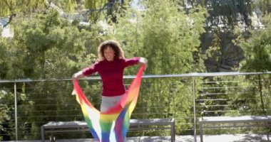 Dışarıda gülümseyen kadın, gökkuşağı bayrağı sallıyor ve güneşli günün tadını çıkarıyor. Gurur, LGBT, mutluluk, kutlama, özgürlük, çeşitlilik