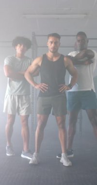 Dikey video: Güvenle ayakta duran, jimnastik salonunda kollarını kavuşturmuş üç adam. Spor, güç, egzersiz, kaslar, antrenman, egzersiz