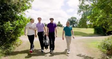 Erkek golfçüler üniforma giyiyor, golf sopalarıyla yürüyor ve güneşli bir günde golf sahasında konuşuyorlar. spor, yaşam tarzı, golf ve etkinlik.