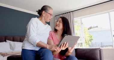 Asyalı büyükanne ve torun tablet kullanıyor, evde birlikte vakit geçiriyorlar. Aile, teknoloji, bağ, eğlence, iletişim, nesiller