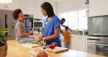 Parlak, modern bir mutfakta farklı bir aile birlikte yemek hazırlıyor. Beyaz dolaplar, paslanmaz çelik aletler, ve büyük pencereler doğal ışığı içeri alıyor, değiştirilmemiş.