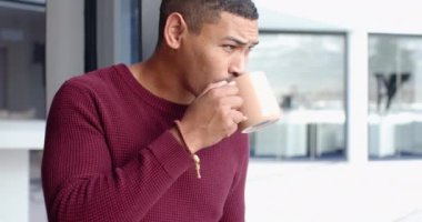 Pencereden dışarı bakan, kırmızı kazaklı adam, arka planda modern bina, kopyalama alanı. Düşünce, şehir, yalnızlık, yansıma, dalgın, mimari