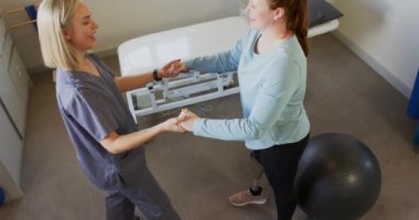 Kafkas protezci, tedavi sırasında protez bacaklı beyaz bir hastaya yardım ediyor. Gri önlük giyen protestan, günlük giyimli hasta, ikisi de egzersize odaklanmış, değişmemiş, yavaş çekim