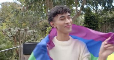 Gurur bayrağına sarılmış gülümseyen genç adam, dışarıda huzurlu bir anın tadını çıkarıyor, kopyalama alanı. LGBTQ, mutluluk, özgürlük, kutlama, kendini ifade etme, çeşitlilik