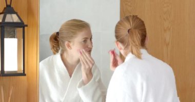 Göz altı bantları uyguluyor, bornozlu kadın banyo aynasına bakıyor. Cilt bakımı, güzellik, kendine bakım, refah, şımartma, sabah rutini, kozmetik, gençleştirme, değiştirilmemiş.,