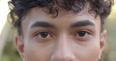 Kıvırcık saçlı, gülümseyen genç adam doğrudan kameraya bakıyor. Portre, mutluluk, kendinden emin, neşeli, arkadaş canlısı, yakın plan