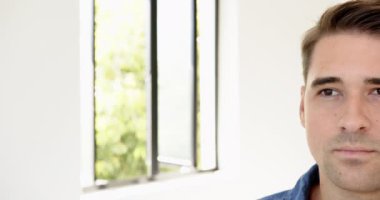 Normal gömlekli gülümseyen adam pencerenin yanında doğal ışıkla duruyor, evde, fotokopi odasında. Portre, yaşam tarzı, kapalı alan, mutluluk