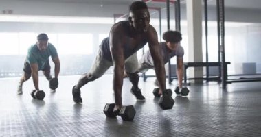 Spor salonunda dambıllı çeşitli gençler antrenman yapıyor, şınav çekiyorlar. Güçlü ve formda Afro-Amerikan bir adam, iki formda çift ırklı adam tarafından takip ediliyor, değiştirilmemiş, yavaş çekim.