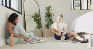 Genç, çok ırklı bir çift yerde oturuyor, ayakkabı giyiyorlar, evde antrenmana hazırlanıyorlar. Fitness, egzersiz, atletik, hazırlık, aktif, yaşam tarzı