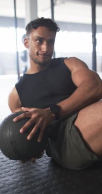 Dikey video: Spor salonunda egzersiz yapmak, sağlık topuyla mekik çekmek. Fitness, egzersiz, güç, dayanıklılık, çekirdek, eğitim