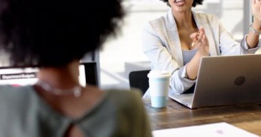 Afrika kökenli Amerikalı ve melez kadınlar iş toplantılarında iş konuşuyorlar. Geniş pencereli parlak bir ofis, masada dizüstü bilgisayar, inceleme için yayılmış kağıtlar, takım çalışması, beyin fırtınası, başlangıç, değiştirilmemiş