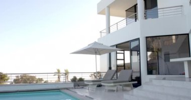 Güneşli bir günde havuz başı şezlongları ve şemsiyeli lüks tatil evi, fotokopi odası. Tatil, dinlenme, kaçamak, seyahat, tatil, gün ışığı