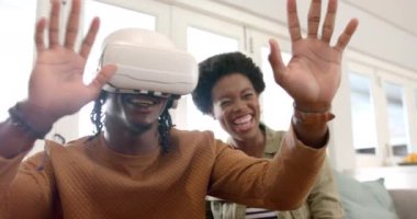 Kadın evde izlerken Afro-Amerikan erkek sanal gerçekliği tecrübe ederek VR cihazını kullanıyor. teknoloji, oyun, eğlence, izleme, etkileşimli, eğlence
