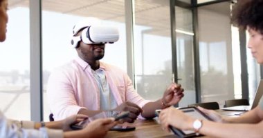 Ofiste VR kulaklıkları kullanan çeşitli iş ortakları. Gri bir geçmişi olan modern bir konferans odasında proje üzerinde işbirliği yapmak, bir başlangıç toplantısına beyin fırtınası yapmak, değiştirilmemiş, yavaş çekim