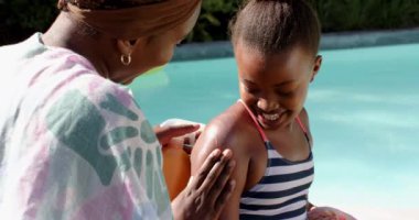 Anne kızına havuz başında güneş kremi sürüyor, güneşli günün tadını çıkarıyor. Ebeveynlik, havuz başı, yaz, aile, boş zaman, değiştirilmemiş, yavaş çekim