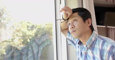 Ekose gömlekli dalgın Asyalı adam pencereden dışarı bakıyor, düşünceleri yansıtıyor, boşluğu kopyalıyor. Düşünce, içgözlem, yalnızlık, yansıma, düşünme, düşünceli.