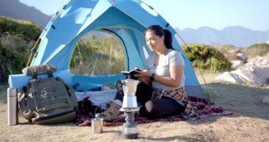 Dağlarda kamp yapmak, kamp malzemeleriyle çadırın yanında kitap okuyan bir kadın. macera, rahatlama, açık hava, doğa, seyahat, rahatlık