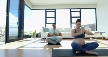 Hamile kadın ve erkek oturma odasında yoga minderleri üzerinde meditasyon yapıyorlar. Meditasyon, rahatlama, refah, doğum öncesi, çift, farkındalık