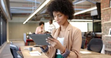 Modern ofiste tablet kullanan melez bir kadın iş arkadaşlarıyla çalışma alanı açıyor. İş hayatına gelişigüzel bir girişimci olarak başlamak, arka planda işbirliği yapmak, dinamik bir ortam yaratmak.