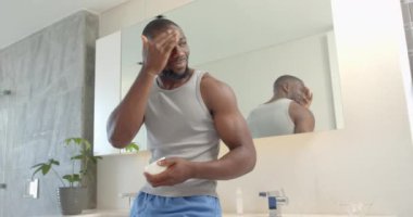 Yüz kremi sürüyorum, güçlü ve formda Afro-Amerikan bir adam evde cilt bakımını seviyor. Kişisel bakım, sağlık, bakım, hijyen, rahatlama, değişmemiş, yavaş çekim