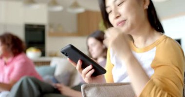 Evdeki koltukta otururken akıllı telefon kullanan gülümseyen kadın. Teknoloji, rahatlama, rahatlama, iletişim, yaşam tarzı, gelişigüzel