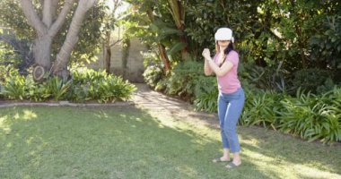 VR kulaklığı kullanan bir kadın, yemyeşil bahçe ortamında sanal gerçekliği keşfediyor. Teknoloji, doğa, yeşillik, dalgın, keşif, dijital